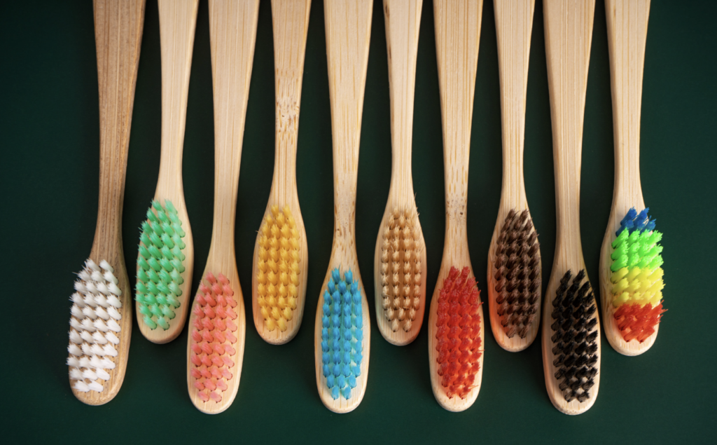 Image of 10 bamboo toothbrushes with colourful bristles lined up on a dark background. Replacing plastic with sustainable materials is key.