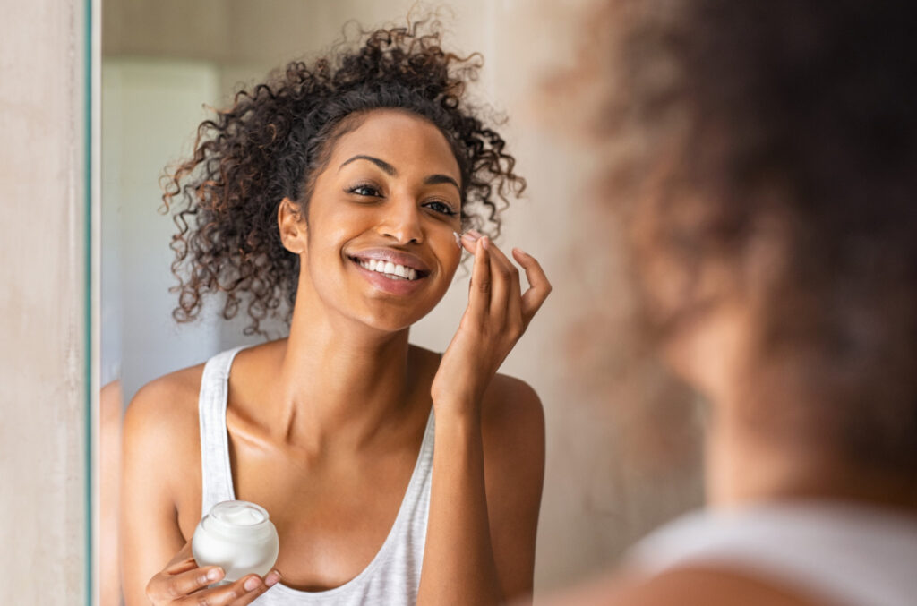 Image of a young women applying lotion to her face in the mirror. Going plastic free in your beauty routine can help you lead a more sustainable lifestyle.