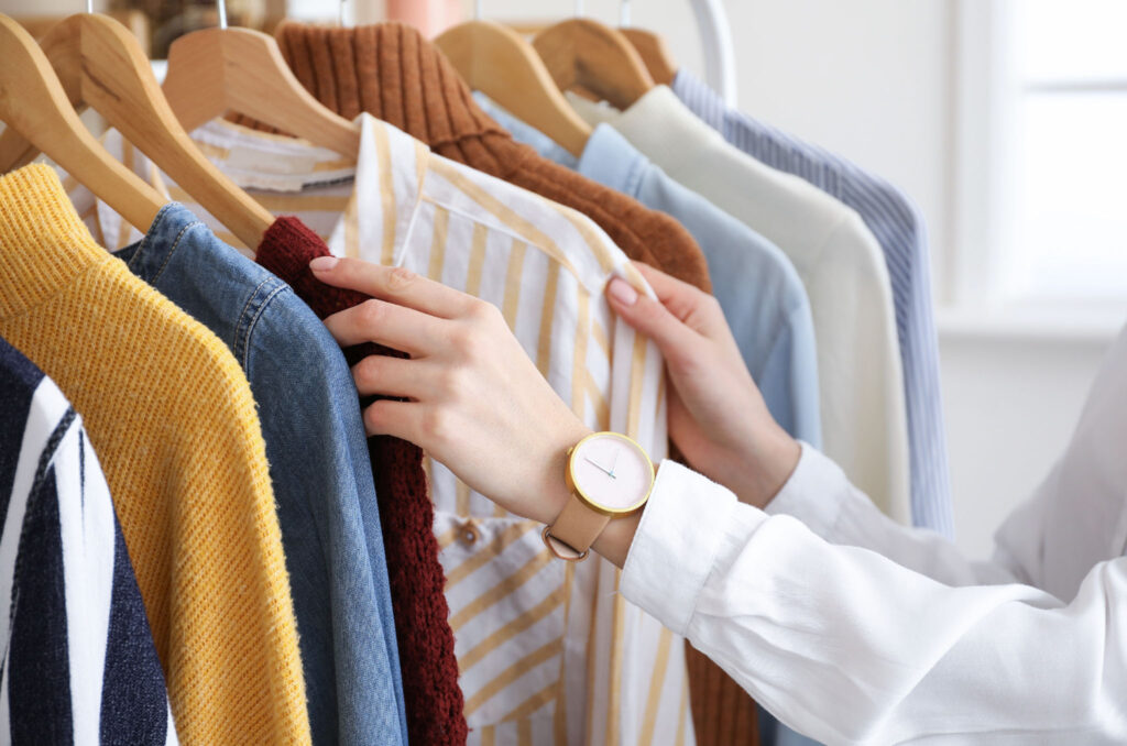 Image of two hands separating articles of clothing hanging on a rack. Choosing sustainable clothing for work can be easy.