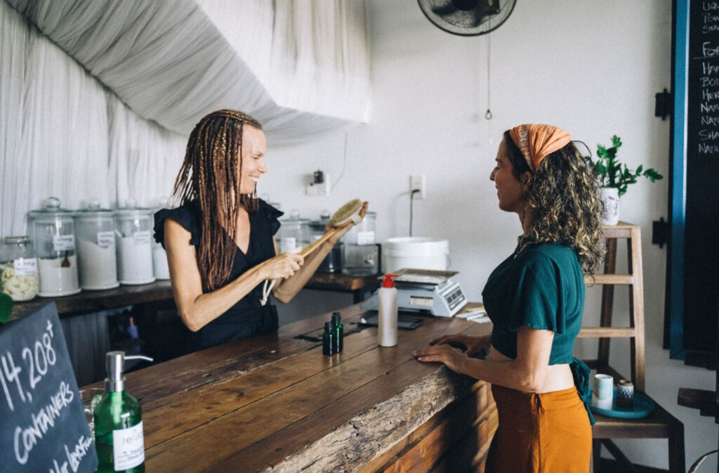 Image of a customer being helped by a shop owner at a counter of a cosmetics store. Supporting brands that are plastic-free and offer product refills is a sustainable option.