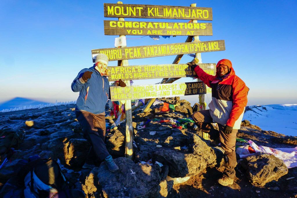 Image of a hiker and their guide at the summit of Mount Kilimanjaro. When opting for ecotourism, make sure to choose sustainable activities and businesses.