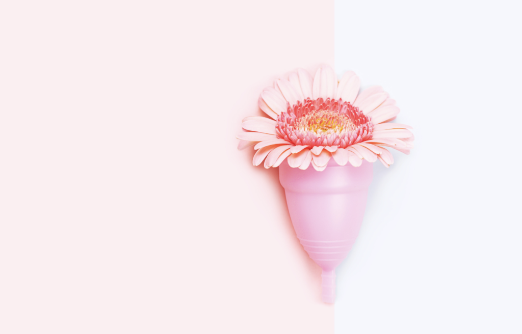 Image of a pink menstrual cup with a pink flower inside. Swapping tampons for a menstrual cup can help you create a plastic-free beauty routine.
