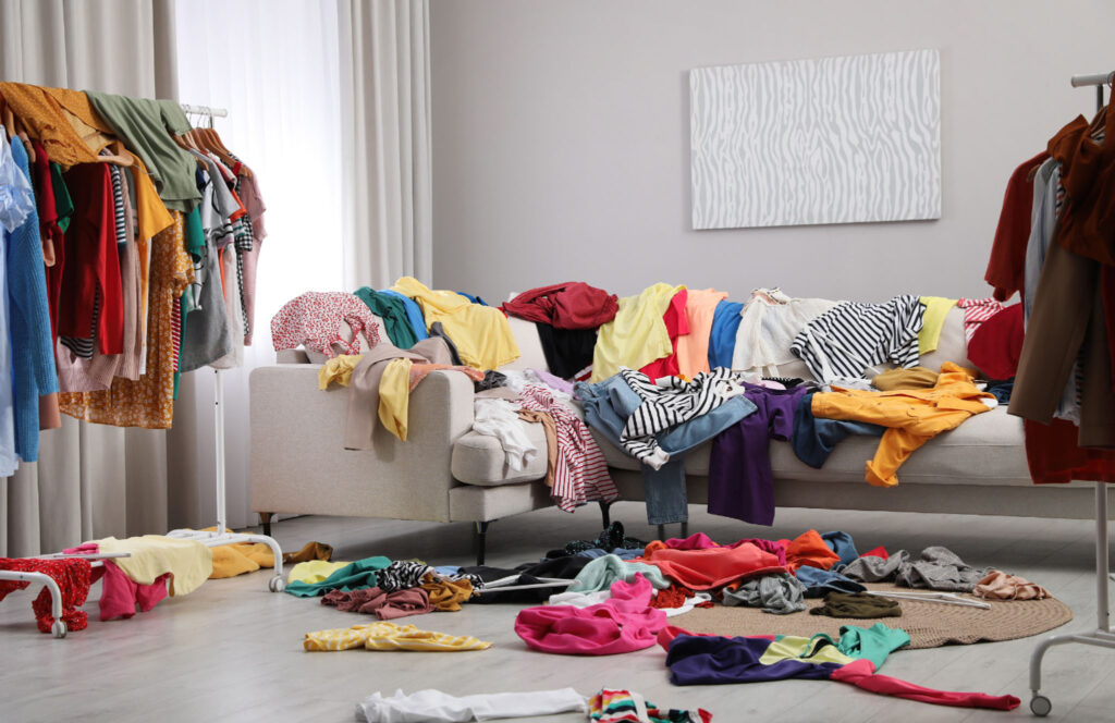 Image of a living room couch, covered in strewn clothing items. Fast fashion has led many of us to own too many clothes we don't even wear.