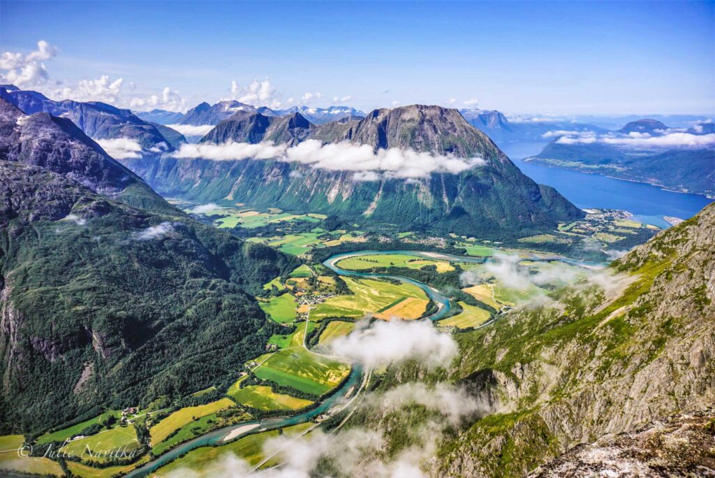 Image from above of a river winding through patches of bright green farmland surrounded by mountains covered in greenery.