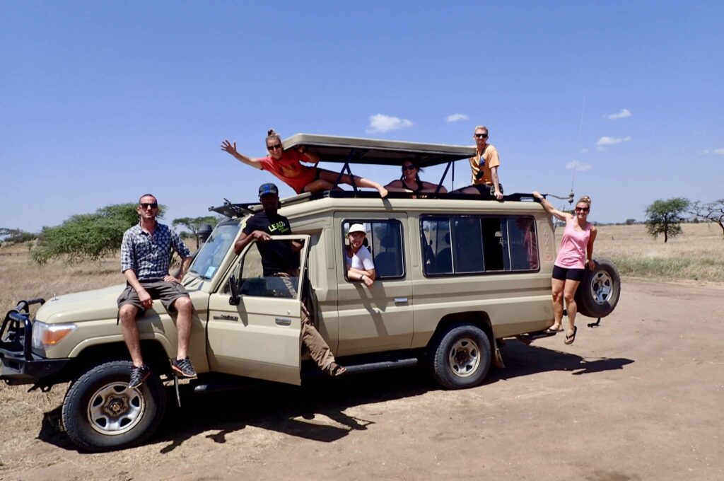 Image of seven people in and on a safari jeep. Choosing sustainable tour operators is important when practicing ecotourism.