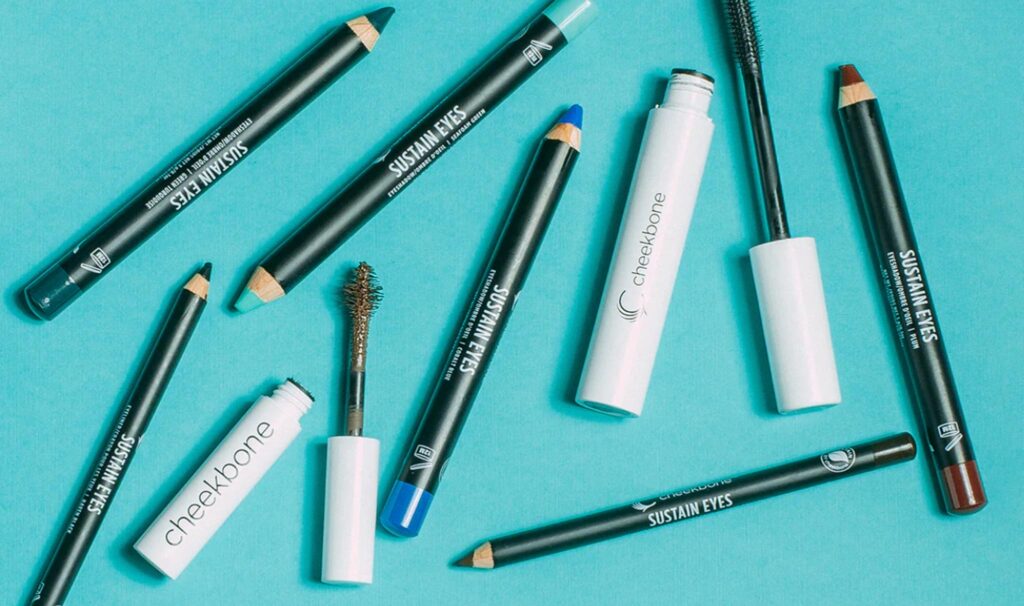 Image of eye liner pencils and mascara from above against a teal blue background. Non-toxic eye makeup is a must in your toiletry bag. 