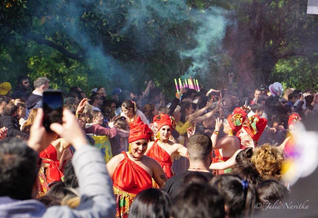Image from within a crowd of spectators at a parade, with traditional candombe dancers at center. Ecotourism can involve cultural activities and learning the history of the area you visit.