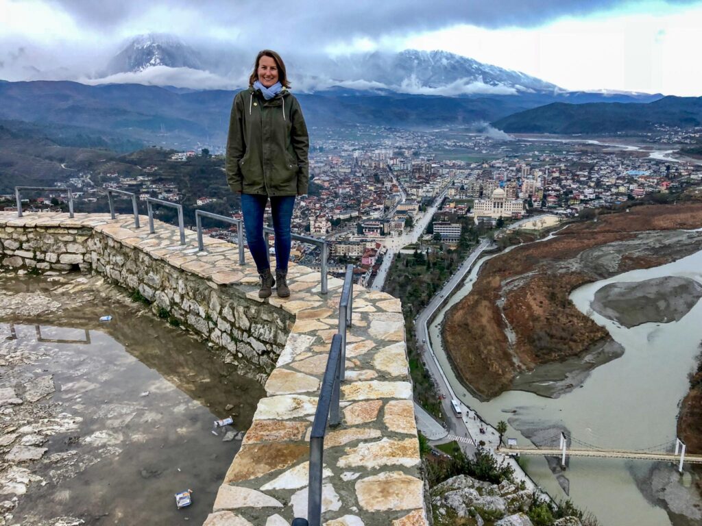 A lone woman stands on a stone wall in front of a view overlooking the city of Berat, Albania.