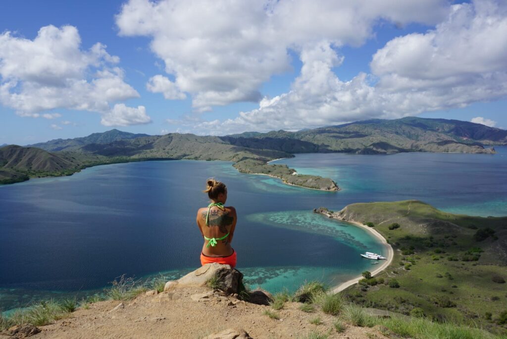 Image of a traveler taken from behind sitting on a ledge overlooking a beautiful turquoise bay in Indonesia.