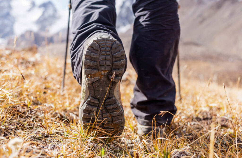 Image of a pair of feet wearing hiking boots walking away from the camera in a grassy area.