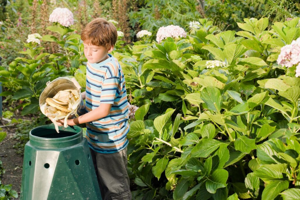 Image of a child emptying food scraps into a compost bin in the yard.