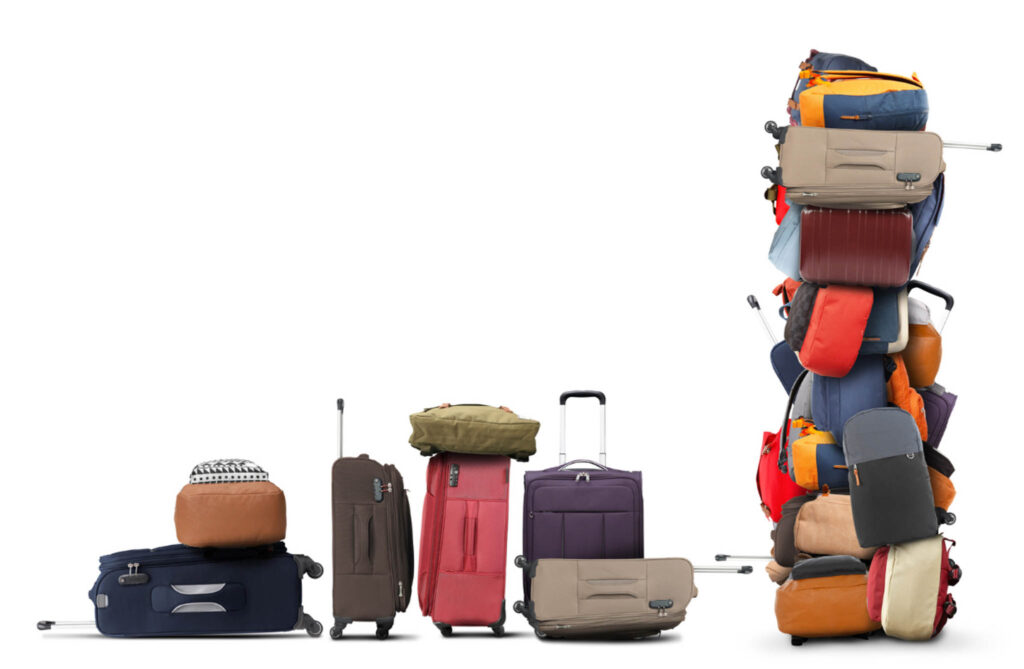 Image of a variety of luggage in haphazard piles. Add sustainable luggage to your "what to pack for a year of travel" list!