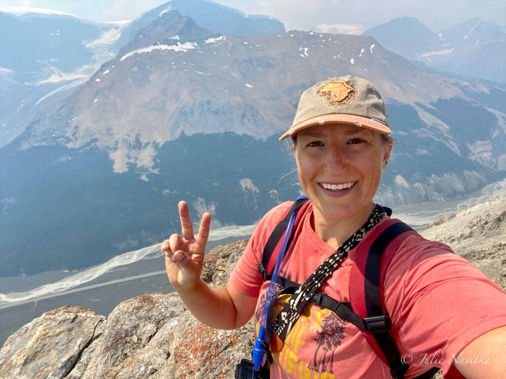 Selfie image of a hiker giving a peace sign at the summit of a mountain.