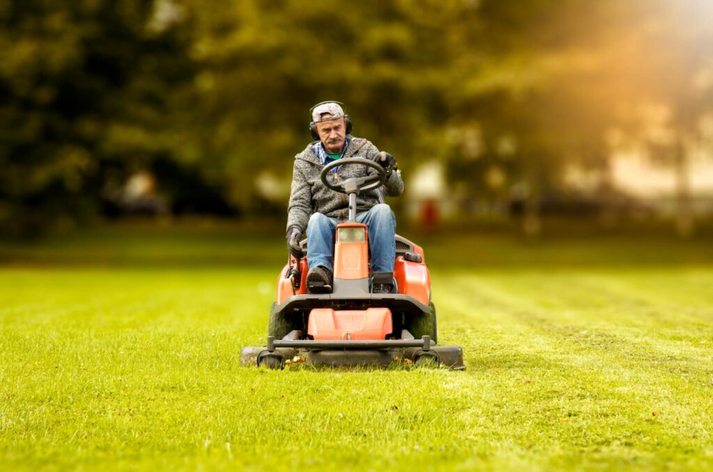 Image of a man riding a lawn mower in a large yard of grass.