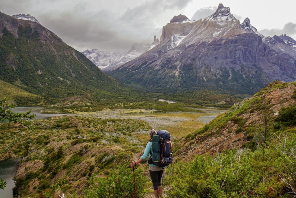 Image of a hiker looking out towards a landscape of mountains and green marshland in Torres del Paine National Park, Chile. Choosing an environmentally-friendly backpack is essential for those that love nature.