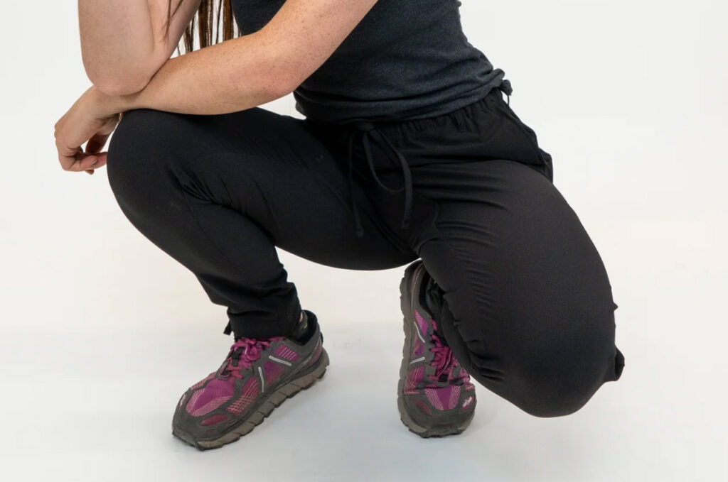 Image of a model crouching in the unisex Trailhead Pants by Coalatree. 