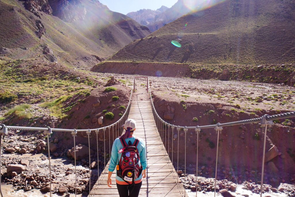 Image of a hiker about to cross a bridge in the mountains of Argentina. A second-hand bag is definitely an environmentally-friendly backpack!