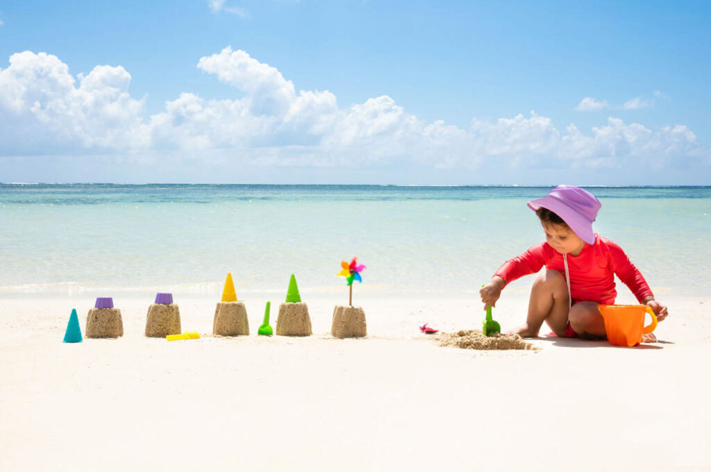 A small child plays alone on the beach building a row of small sand castles. Choosing eco-friendly beach toys can help you practice sustainable recreation.
