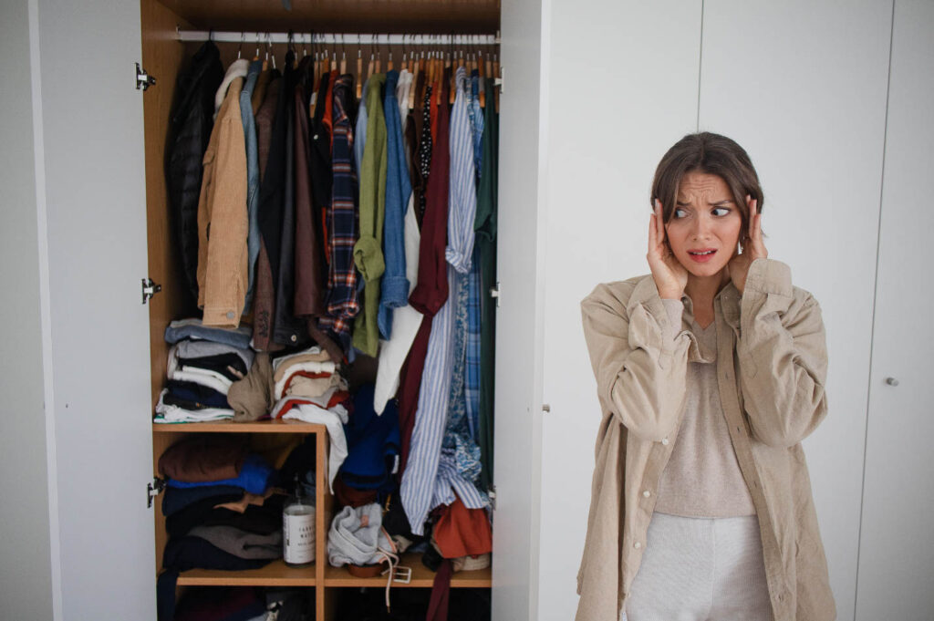 Image of a woman who appears to be stressed standing outside a cluttered closet.
