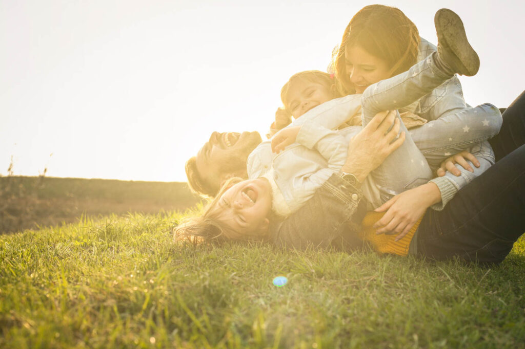 Image of a family of four rolling around laughing on the grass in golden rays of the sun.
