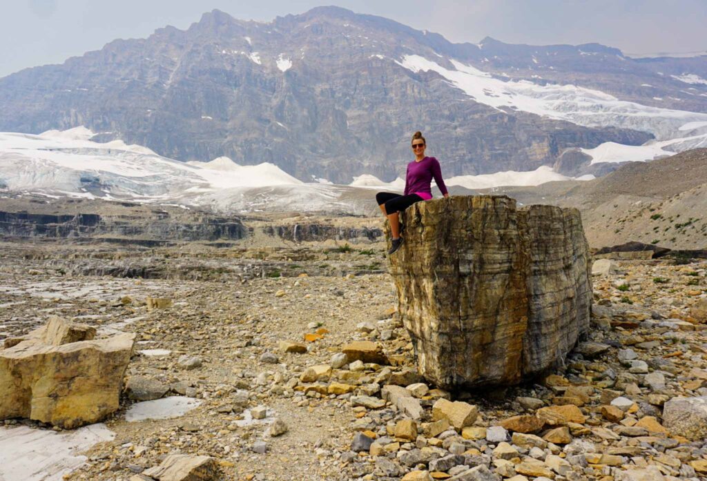 Image of a hiker sitting atop a large boulder with mountains in the background. Building a sustainable hiking capsule wardrobe can be quite easy!