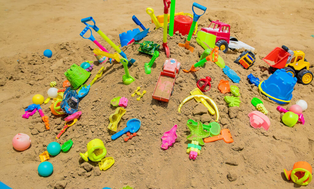 Image of many plastic beach toys with small parts laying on the sand.