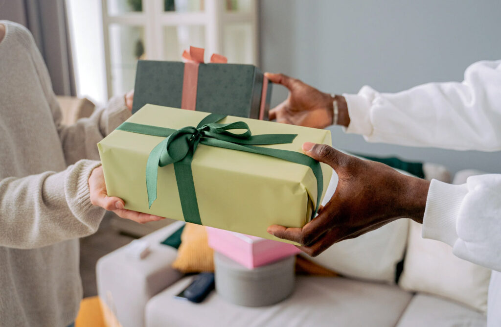Image of two pairs of hands exchanging nicely wrapped gifts. There are many ways to give more eco-friendly gifts.