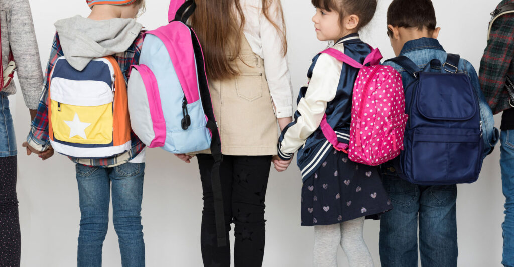 Image of a group of children wearing backpacks and holding hands taken from behind. Teaching our kids about sustainability is easy when we buy an environmentally-friendly backpack together!