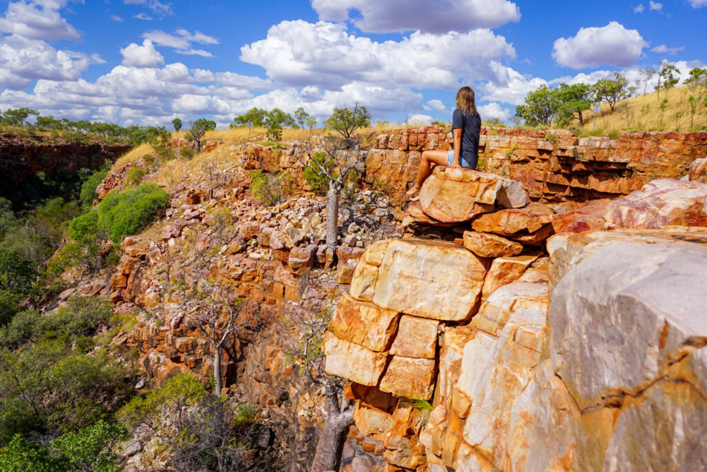 Image of a hiker sitting on a rocky outcrop overlooking a canyon landscape in Australia. Sometimes your hiking capsule wardrobe doesn't even call for shoes!