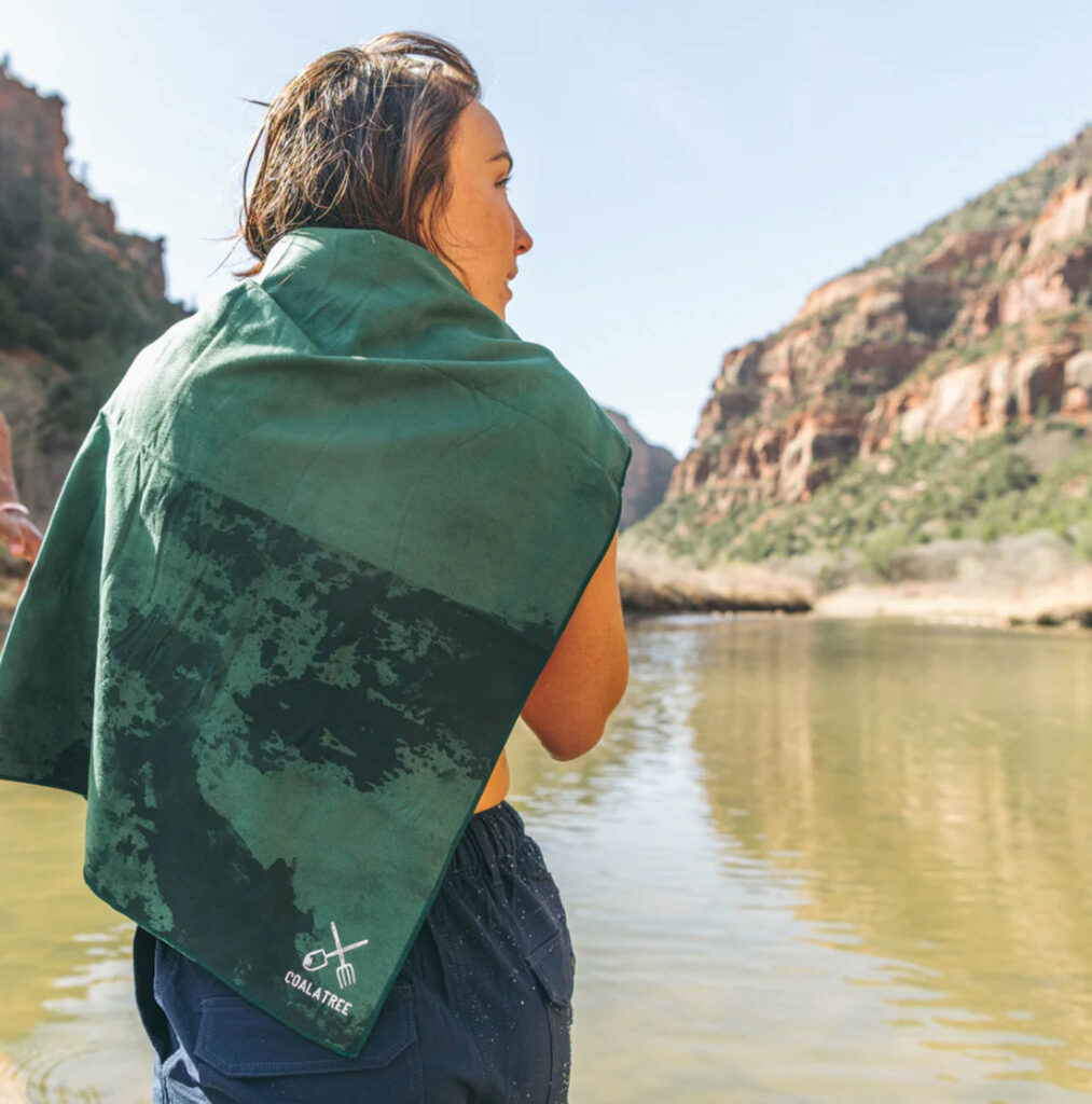 Image of a woman wearing the Microfibre Towel from Coalatree on her shoulders near a lake.