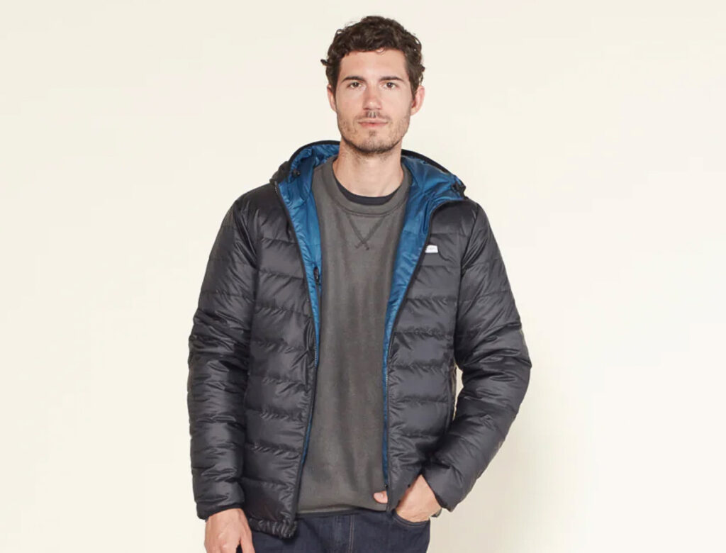 Image of a model wearing the reversible Outerknown Hooded Puffer. A lightweight and packable down or synthetic puffer jacket is a staple in a hiking capsule wardrobe.