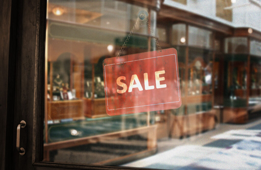 Image of a storefront window with a hanging sale sign. Keeping an eye out for sales from eco-friendly brands can help you shop sustainably on a budget.