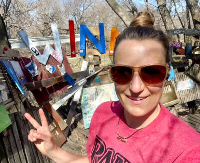 Image of a runner giving the peace sign in front of an art installation in a park.