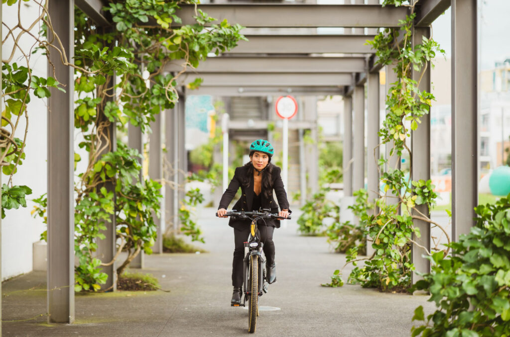 Image of a cyclist wearing office attire biking through a corridor covered in vines. Cycling to work is one way to become a green commuter!