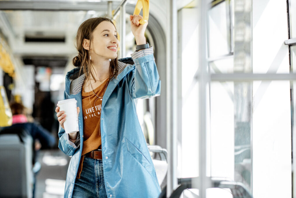 Image of a young woman holding a coffee riding on public transportation.