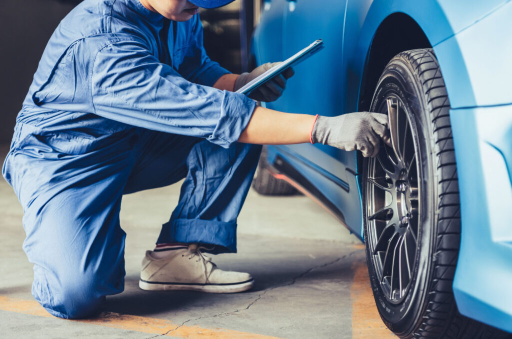 Image of a person kneeling and checking the air pressure on a car tire. Maintaining your vehicle makes it more fuel efficient for an environmentally friendly work commute.