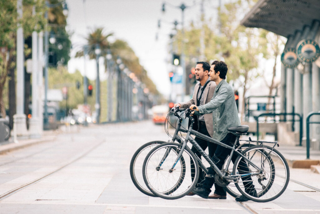Image of two people wearing office attire crossing the street with bikes on their way to work.