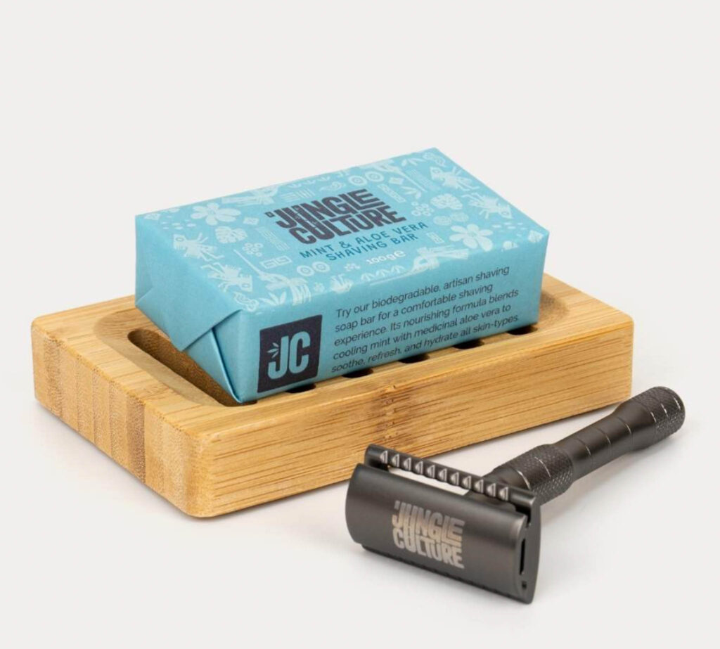 Image of the Tip-to-toe shampoo and shave bar from Jungle Culture sitting on bamboo soap shelf next to a safety razor.
