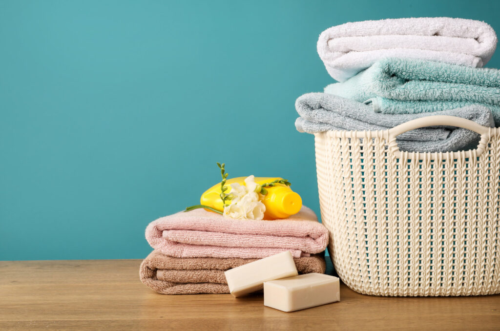 Image of a laundry basket filled with clean towels on a countertop beside more folded towels.