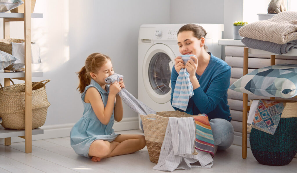 Image of a mother and daughter sitting on the laundry room floor folding clothes and enjoying their scent.
