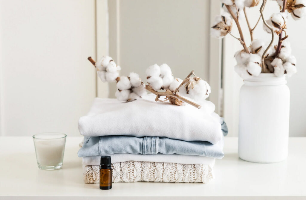 Image of fresh folded and fluffy towels on a countertop beside a vase of branches with cotton buds.