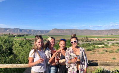 Image of four women holding wine glasses in front of a vista of greenery in the Cederberg Mountains, South Africa.