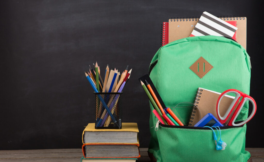 Image of a backpack brimming with sustainable school supplies next to a cup full of pencils sitting atop a pile of books.