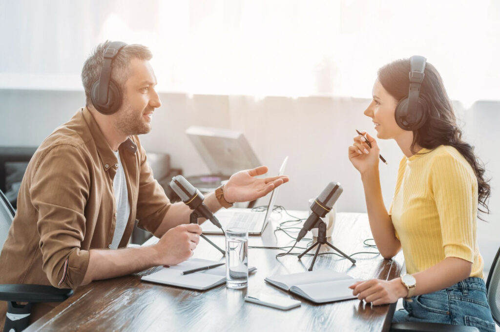 Image of two people wearing headphones sitting across a table from each other engaged in conversation. Podcasts about sustainable recreation are a good choice for nature lovers!