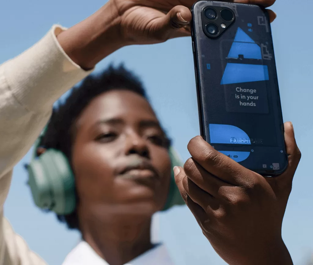 Image of a person wearing headphones holding up the latest eco-friendly mobile phone, Fairphone.