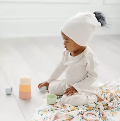 Image of a small toddler wearing a white hat with pom pom.