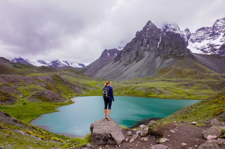 Image of the author of website standing on a boulder in front of a panoramic view over a turquoise lake in the mountains of Peru.