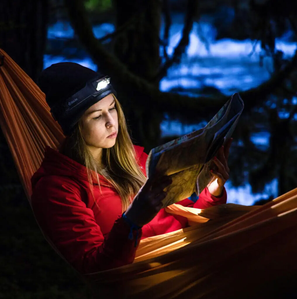 Image of a women in a hammock using the Biolite 325 headlamp to look at a map at night.