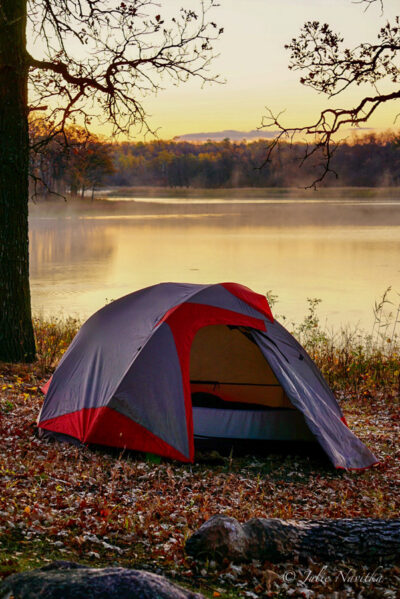 Image of a tent set up in front of a lake at sunrise.