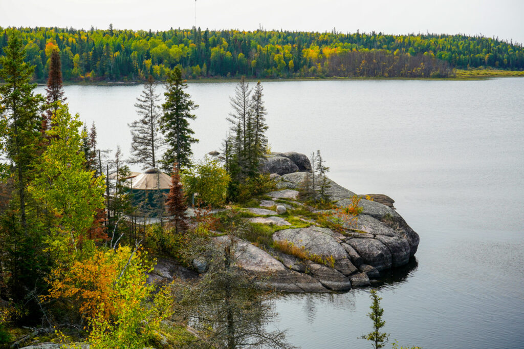 Image of a yurt on a peninsula of a lake in autumn, taken from above at a distance.